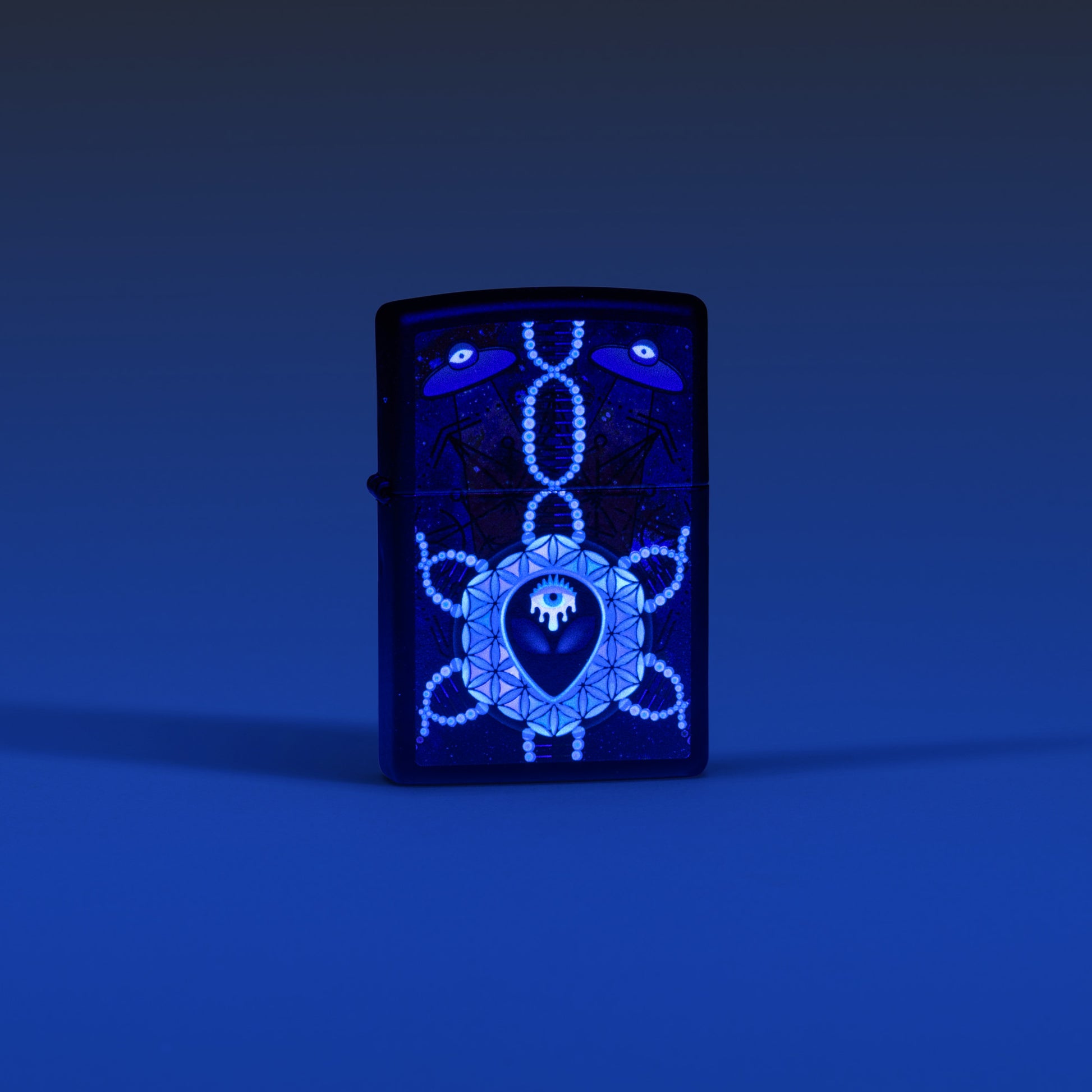 Lifestyle image of Zippo All Seeing Alien Design Black Matte Windproof Lighter glowing in the dark with a blue ombre background.