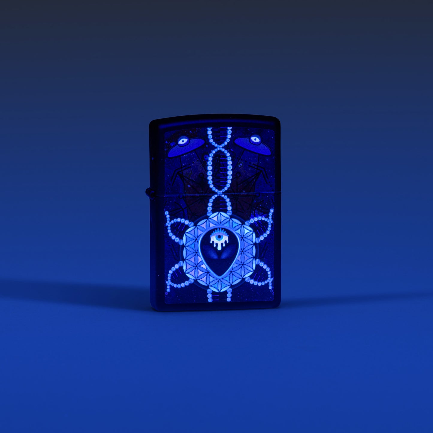 Lifestyle image of Zippo All Seeing Alien Design Black Matte Windproof Lighter glowing in the dark with a blue ombre background.
