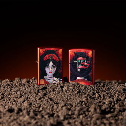 Lifestyle image of two Zippo Dinner for Two Design Metallic Red Windproof Lighters; one showing the front of the lighter and the other showing the back of the lighter, both standing in dirt with a black and orange ombre background. 

