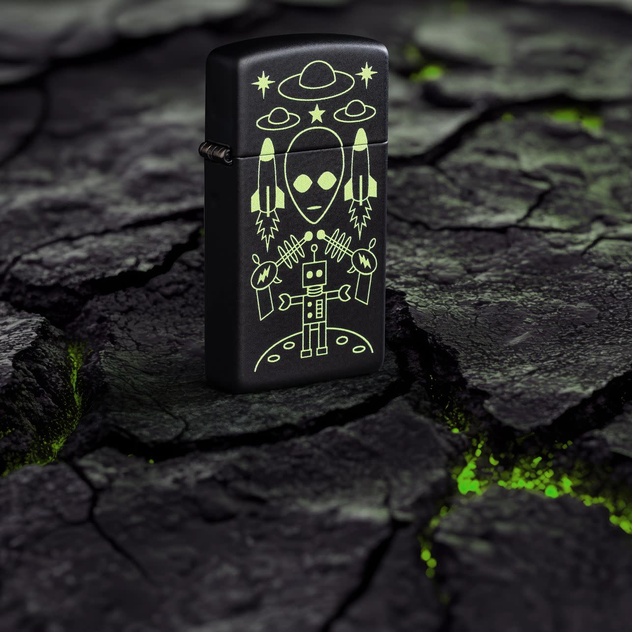 Lifestyle image of Zippo Alien Invasion Design SlimÂ® Black Matte Windproof Lighter standing on blacktop with green glowing cracks.